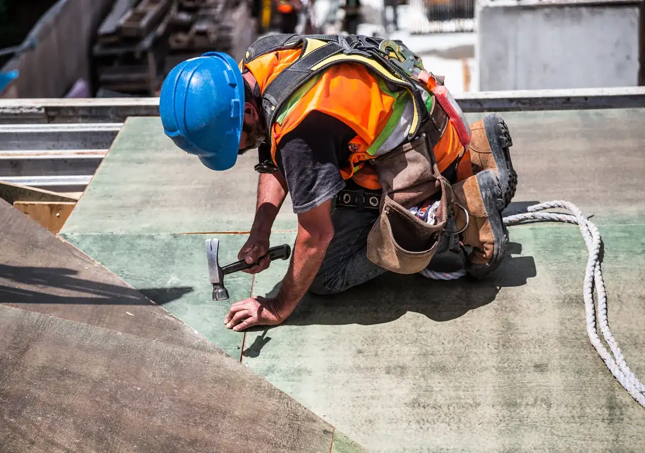 A roofer in a hard hat fixing roof boards with a hammer