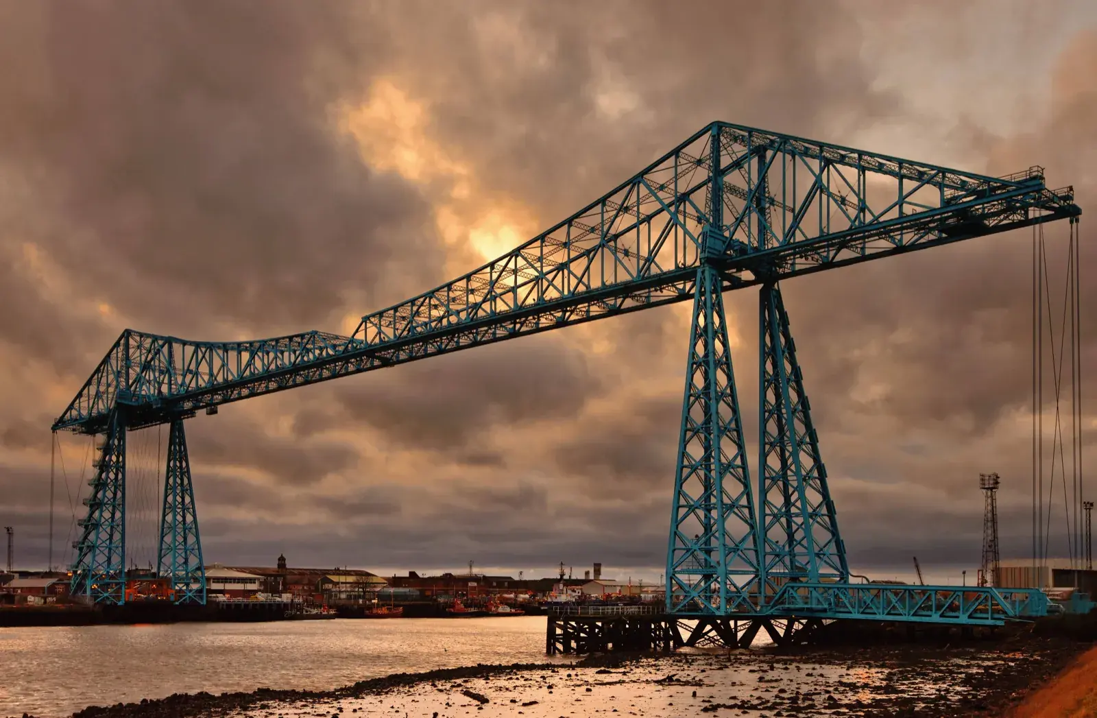 The Tees Transporter Bridge in Middlesbrough, its blue steel towers and high girder against a cloudy sunset sky.
